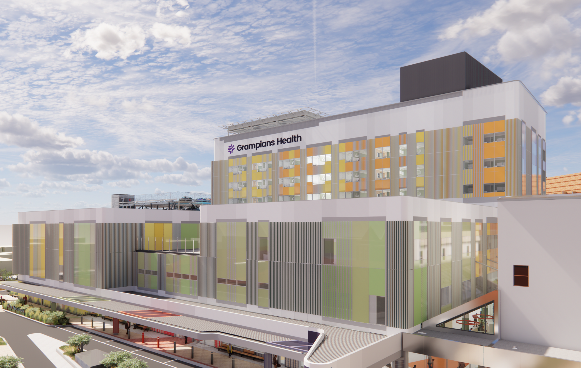 Modern hospital building labeled "Grampians Health" featuring glass and metal panels with green and orange accents. Multi-level structure includes a drive-up entrance area. Partly cloudy sky enhances the bright, clean appearance.