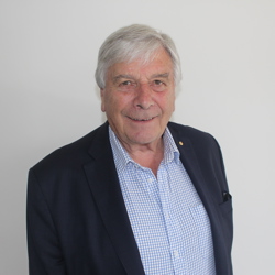 Rob Knowles 54531924371 O A person with grey hair is wearing a dark blazer over a light blue checkered shirt. The background is plain and white.