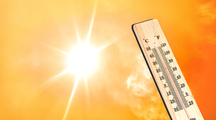 Bright sun shining in an orange sky with a wooden thermometer showing high temperatures in both Celsius and Fahrenheit