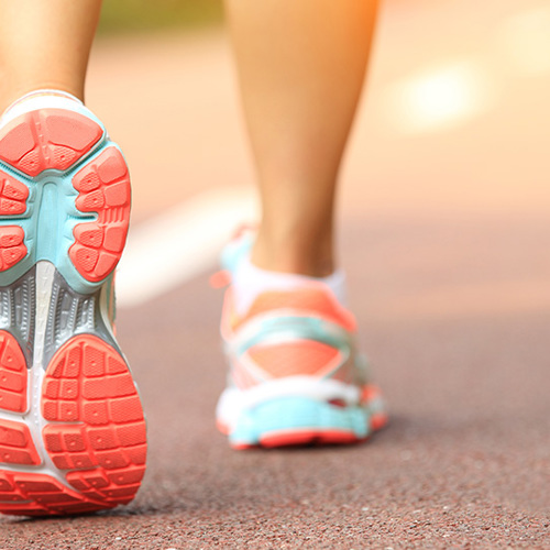 Ladies lower legs wearing trainers with orange, blue and white soles, walking on a track 