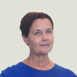 A person with short, dark hair wearing a blue top and the background is plain and light-colored.