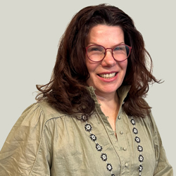 Cora Trevarthen 52482176742 O A person with shoulder-length dark hair wearing a light green blouse with puffed sleeves and floral embroidery along the button placket. The background is plain and light-colored.