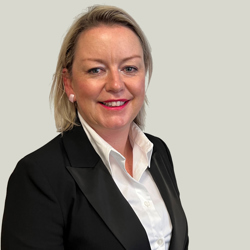 Rhian Jones 52483138115 O A person with shoulder-length blonde hair wearing a black blazer over a white dress shirt. The background is plain light gray.