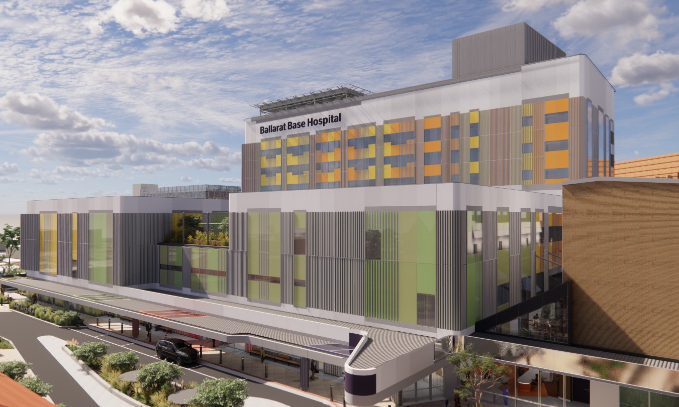 Modern hospital building labeled "Ballarat Base Hospital" featuring glass and metal panels with green and orange accents. Multi-level structure includes a drive-up entrance area. Partly cloudy sky enhances the bright, clean appearance.