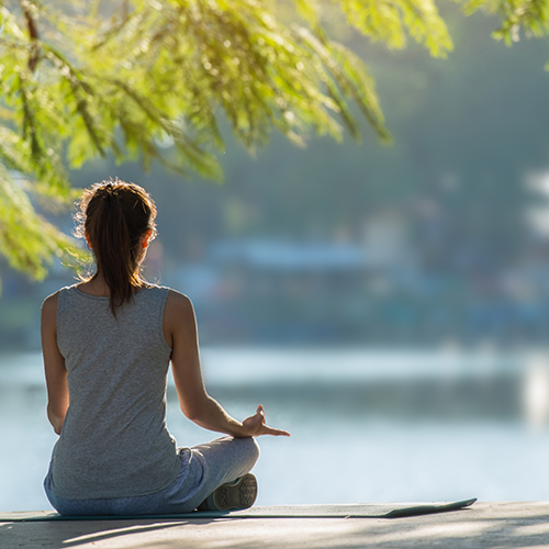 Woman sitting with legs crossed looking out to a lake while sitting under a tree.